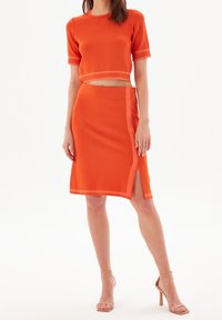 Oranžový pletený dvoudílný outfit s cropped topem s krátkými rukávy a sukní ke kolenům se bočním rozparkem a kontrastním lemováním.