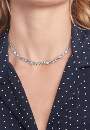 Collier à double chaîne en argent porté par une personne vêtue d'une chemise à col bleu marine à pois.