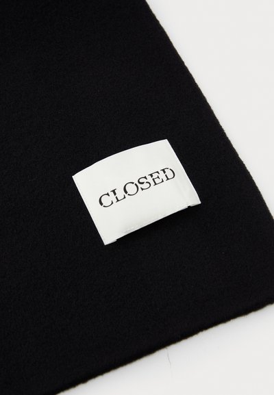 Fekete szövet, puha tapintással, amelyen egy fehér címke található, rajta vastag fekete betűkkel a "CLOSED" felirattal. A címke biztonságosan bele van varrva a szövetbe.