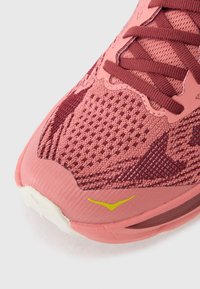Pink athletic shoe with textured mesh upper, darker rose accents, and contrast yellow logo. Rounded toe and cushioned sole design.