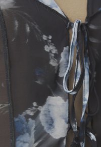 Blouse kukkakuosisella mustalla kankaalla, jossa on sinisiä ja valkoisia kukkia, säädettävät kaulaketjut ja kontrastivärinen musta reunus.