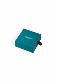 Scatola rettangolare color verde smeraldo con chiusura magnetica, presenta un logo a forma di ala argentata sulla parte superiore e una linguetta in tessuto nero sul lato.