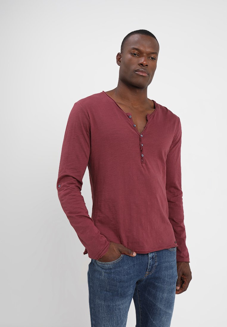Langärmliges burgunderfarbenes Henley-Shirt mit lockerer Passform, strukturiertem Stoff, fünf Knöpfen am Hals und angenähtem, knöpfbarem Ärmel-Detail.