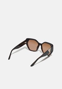 Ochelari hexagonali cu ramă din tortoiseshell închis și lentile maro. Dispune de accente aurii pe tâmple. Textură netedă cu un finisaj lucios.