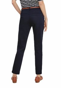 Pantaloni blu navy dal taglio slim, caratterizzati da una texture morbida, due tasche posteriori e una cintura in pelle marrone. Progettati con un aspetto pulito e su misura.