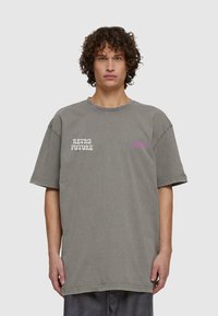 Pārmērīgi liels pelēks kokvilnas T-krekls ar priekšā tekstu "RETRO FUTURE" balta krāsā un mazu rozā logotipu, apļveida kakla izgriezumu un īsām piedurknēm.