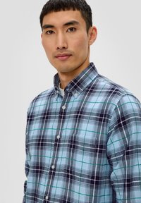Camicia a maniche lunghe a quadri con motivi blu, neri e verdi. Presenta un colletto, una fila di bottoni e una tasca sul petto. Tessuto in cotone.