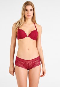 Rode kanten beha met padded cups en verstelbare banden, gecombineerd met bijpassende sheer kanten boyshorts met golvende randen en een klein strikdetail.