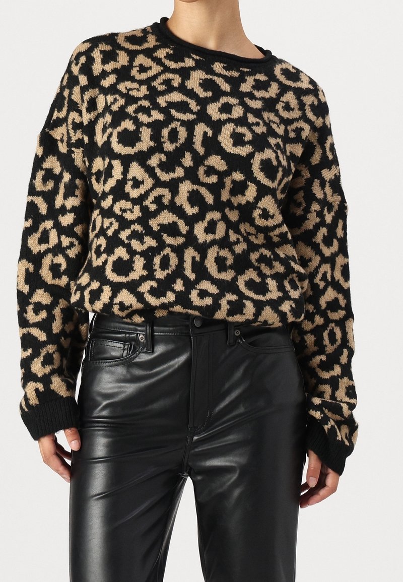 Pull imprimé léopard en maille noire et beige, avec une coupe décontractée et des poignets côtelés, assorti à un pantalon en cuir noir taille haute.