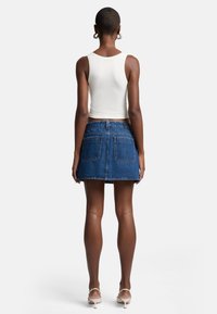 Jupe A-line en denim avec coutures visibles, deux poches arrière et un ourlet brut. Associée à un débardeur blanc ajusté.