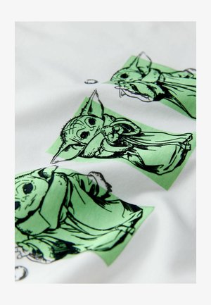 Weißer Stoff mit wiederholten schwarzen und grünen Illustrationen einer Figur mit großen Ohren, die einen Gegenstand hält und einen Umhang trägt.