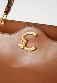 Brown leather handbag with a shiny gold C-shaped clasp, featuring a smooth texture and scalloped edges. Elegant design and sturdy hardware.