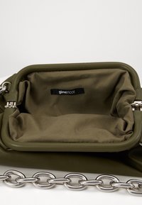 Wnętrze zielonej torebki z ekoskóry z miękką podszewką, z czarną metką oraz srebrnym łańcuszkiem na zewnątrz.