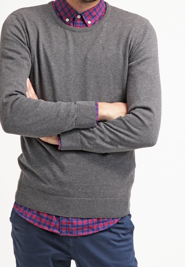 Grauer Strickpullover mit runder Ausschnitt, getragen über einem rot-blauen karierten Hemd. Enthält gerippte Bündchen und Saum und zeigt einen geschichteten Stil.