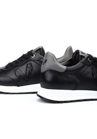 Baskets en cuir noir avec une surface texturée, accents gris, semelle blanche et détail de logo sur les côtés. Design minimaliste avec fermeture à lacets.