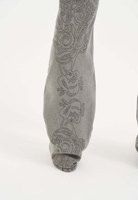 Pantaloni in cotone grigi caratterizzati da ricami tonali dettagliati con motivi a spirale e floreali lungo i lati, con caviglie affusolate.