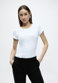 Λευκό εφαρμοστό κοντομάνικο μπλουζάκι με στρογγυλή λαιμόκοψη, σε συνδυασμό με ραμμένο μαύρο παντελόνι. Λείο ύφασμα με κομψό σχέδιο.