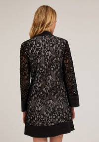 Abito in pizzo nero con un design a motivi, colletto e polsini neri uni. Il tessuto ha una texture trasparente ed è aderente.