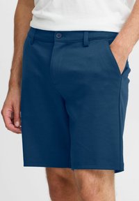 Marineblå shorts laget av glatt stoff, med knappelukking, sidelommer og en tilpasset passform som når rett over kneet.