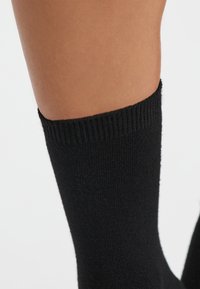 Calcetín negro hasta la rodilla, hecho de material de punto acanalado, que presenta una textura suave y un ajuste ceñido alrededor de la pantorrilla. Sin patrones o acentos visibles.