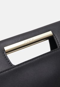 Mustan nahkainen käsilaukku, jossa on kultasävytteinen metallikahva, jossa on kaiverrettu "FURLA". Sujuva pinta ja minimalistinen muotoilu.