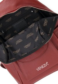 Indvendig i den røde lædertaske er der en sort foring med gentagne Venezia-branding. Lynlås lomme og struktureret læder er synligt.