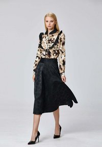 Blouse à motifs floraux avec des détails en volants, associée à une jupe midi noire au design texturé et à des escarpins noirs élégants.