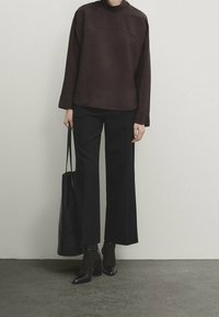 Top marrone scuro con collo alto e vestibilità ampia, abbinato a pantaloni neri a gamba larga e stivali con tacco neri. Porta una borsa a tracolla nera.