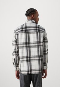 Tjekket flannel skjorte i hvid, sort og lys grå. Har lange ærmer, en spids krave og knapmanchetter. Blød tekstur.