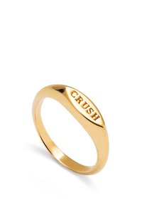 Anillo de metal dorado con una superficie lisa y pulida, de banda ovalada y con la palabra "CRUSH" grabada en la parte frontal.