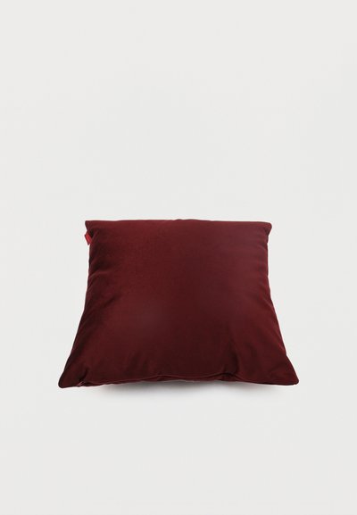 Coussin carré en velours rouge foncé à surface lisse, placé sur un fond clair uni.