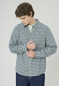 Chemise à boutons vérifiée en bleu marine et crème, avec un col, des manches longues et des boutons en bois, dotée d'une coupe décontractée et d'une texture douce.