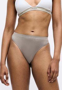 Calvin Klein højtaljede trusse i en neutral beige farve. Glat stof med diskret branding på taljen og sømløst design for komfort.
