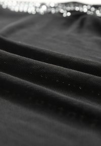 Black fabric with a textured surface, featuring subtle sparkling accents along the edge, creating a layered effect.