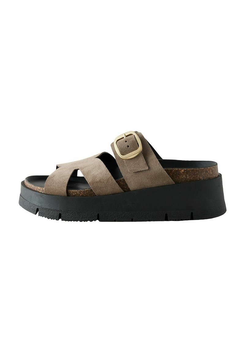 Sandalia de ante en taupe con un diseño de tiras cruzadas, que presenta un detalle de hebilla dorada. Suela de plataforma de goma negra gruesa con textura.