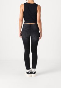 Top de tirantes negro corto combinado con jeans ajustados negros de cintura alta. Características notables incluyen bolsillos traseros y dobladillo desgastado. Llevado con zapatillas negras.