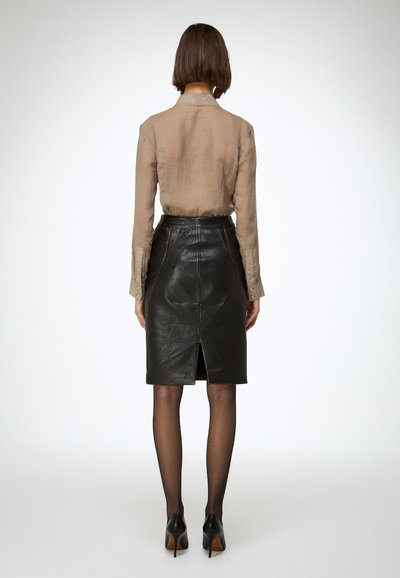 Világos bézs áttetsző blúz és fekete bőr ceruzaszoknya hátul hasítékkal, fekete magassarkú cipővel és áttetsző harisnyával párosítva.