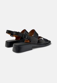 Sandalias de cuero negro con parte trasera cerrada, correa ajustable con hebilla, diseño de punta abierta y suela gruesa negra.