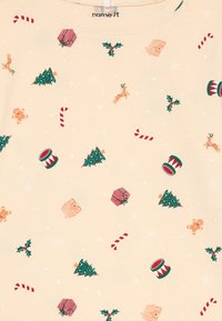 Tela beige con motivos navideños dispersos que incluyen bastones de caramelo, árboles de Navidad, tambores, acebo, regalos, hombres de jengibre, renos, copos de nieve y casas.