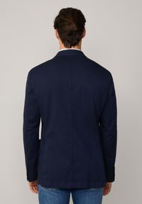Marineblaue Baumwoll-Blazer mit einem einzelnen Rückenschlitz, spitzen Revers und geknöpften Manschetten, kombiniert mit hellblauen Jeans.