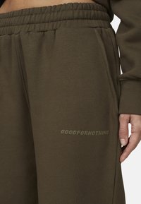 Olive zielone spodnie dresowe o luźnym kroju, z elastycznym pasem i bocznymi kieszeniami. Napis "GOODFOR NOTHING" wytłoczony na nogawce.