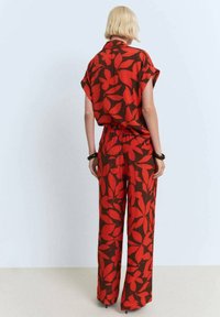 Red and brown floral patterned outfit with a loose, short-sleeved top and wide-leg pants, featuring an elastic waist and smooth fabric texture.