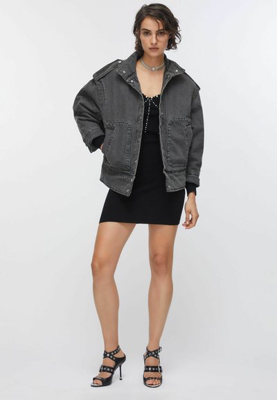Veste grise surdimensionnée avec un col structuré, deux poches avant, associée à une robe noire côtelée et des sandales noires à talons hauts et à lanières.
