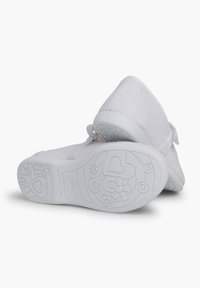 Zapatos de tela blanca con superficie texturizada, correa de velcro y suela de goma con patrones de corazones y flores en la parte inferior.