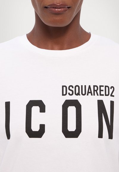 Valkoinen puuvillatee-paita, jossa on rohkea musta "DSQUARED2" -teksti "ICON"-sanan yllä suurilla lohkokirjaimilla. Pyöreä kaula-aukko ja pehmeä tekstiili.