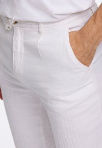 Pantalones de lino blancos con un corte relajado, que cuentan con bolsillos laterales y una tela texturizada. La cinturilla incluye un detalle de cordón para ajustar.