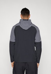 Μπλε ναυτικό και γκρι μπουφάν με κουκούλα, κατασκευασμένο από ελαφρύ υλικό με μακριά μανίκια. Διαθέτει ετικέτα με λογότυπο στην πλάτη και γκρι πάνελ ως διακοσμητικά στοιχεία.