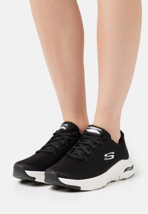 Black mesh sneakers with white sole, lace-up design, padded ankle, and "S" logo on the side. Textured upper and lightweight construction.