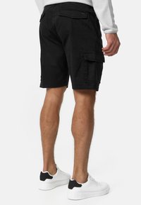 Shorts cargo noirs avec poches latérales et rabats arrière, en coton, longueur au genou, assortis à des baskets blanches avec des accents noirs.