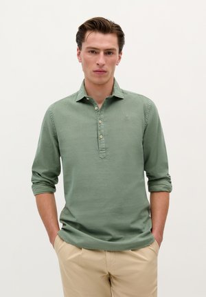 Groen shirt met lange mouwen, een kraag, een placket met drie knopen en een subtiele textuurstof. Gekozen met beige broek.